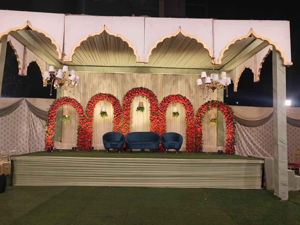 Stage with floral arches and seating set up under a tent by Negi Catering